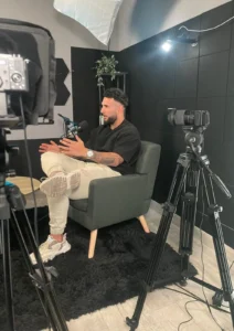 Una persona habla sentada en el sillón del set entre dos cámaras sobre trípode, iluminada por dos softbox