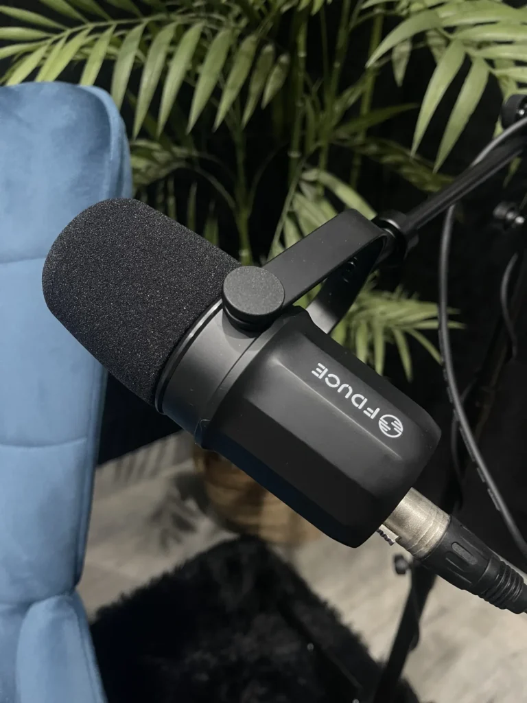 Detalle de un micrófono dinámico con espuma antiviento sobre un sillón azul del set