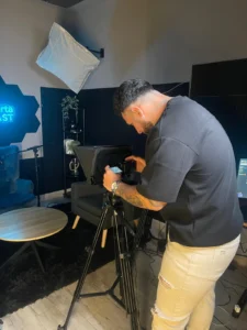 Una persona de espaldas ajusta los controles de la cámara con teleprompter montada sobre trípode en el set