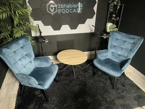 Dos butacas de terciopelo azul enfrentadas con una mesa redonda de madera, ante el mural acústico hexagonal con el rótulo de neón de Zonabierta